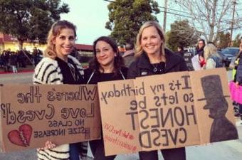 教育工作者微笑着站在学校附近举着抗议标语支持CVESD