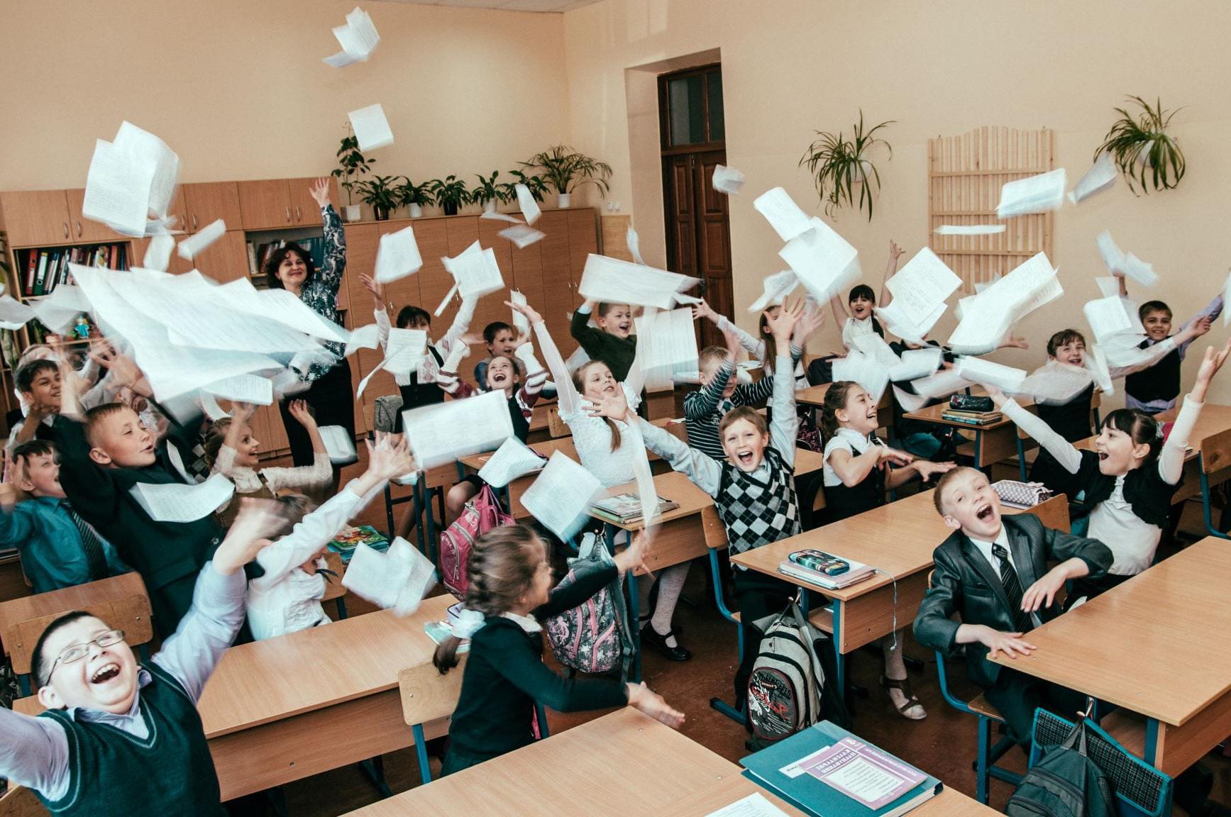 教室里的学生笑着，和老师一起把纸扔到空中