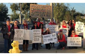 外面的人们都穿着红色的衣服，举着抗议标语，支持赛普拉斯教师博览会的合同